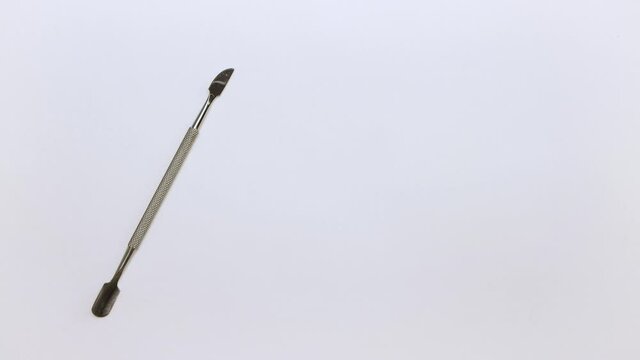 A man's hand places a metal manicure spatula on the table on the left. There is a place to insert text. Self-care nails. Isolated video on a white background. Close-up. Warm, soft light. UHD.