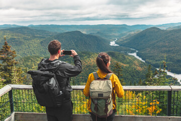 Hikers couple camping walking with backpacks in Quebec National Park taking picture of view with...