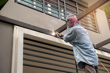 A man holding a welding machine and doing spot welding under the canopy of his garage. Sparks fly away. No protective gloves on hands.