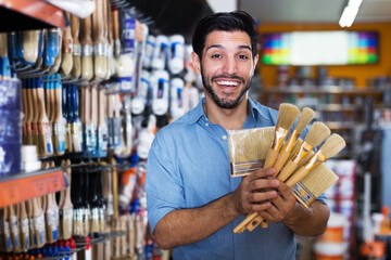 Cheerful man choosing tools for home renovation in paint shop