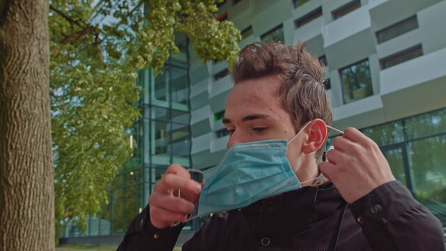 SLOW MOTION, CLOSE UP, PORTRAIT, OF: Cheerful Caucasian man removes his protective face mask at end of the coronavirus pandemic. Guy standing in the middle of the street takes off his surgical mask