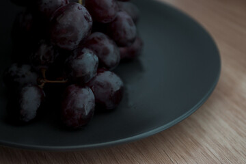 Close-up of grapes with water droplets on a black ceramic plate.
