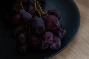 Close-up of grapes with water droplets on a black ceramic plate.