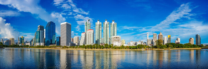 Panorama view of Bangkok city skyline reflected on a lake on a sunny day. Bangkok, Thailand.