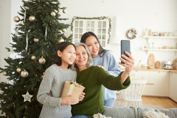 Happy mother making selfie portrait on mobile phone together with her two daughters during Christmas Day