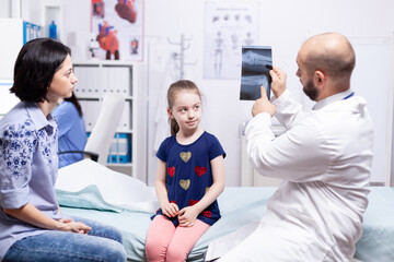 Obraz premium Doctor with mother and child looking at radiography in hospital office. Healthcare physician specialist in medicine providing health care services treatment examination.