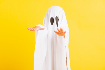 Funny Halloween Kid Concept, Closeup a little cute child with white dressed costume halloween ghost scary, studio shot isolated on yellow background