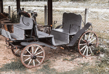 A self-made wagon made of wood and metal with wooden wheels is parked under a canopy, enclosed by a net.