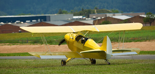 Yellow light biplane parked on green field on aerodrome