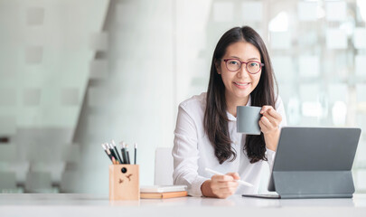 Obraz premium Young asian woman drinking and relaxing while working at office.