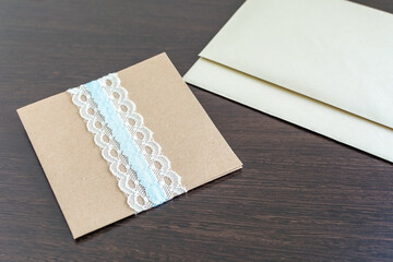 Handmade decorative envelope with two empty paper sheets on the wooden table. Rough paper templates for manuscript with copy space. Office present mockup on the dark surface.