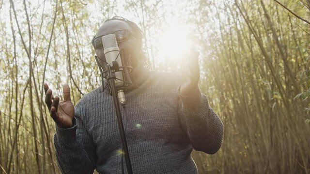 Young affrican man singing in the nature, sun rays coming through the trees