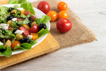 On the kitchen board is a white plate with a vegetable vitamin salad made from tomatoes, olives, lettuce leaves and olive oil.