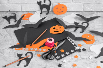 Decoration for the holidays, cutting from colored paper on a white concrete table. Preparation for Halloween. Orange and black colored paper, scissors, pencils, figured hole punch.