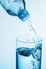 Pouring water from a bottle into glass on a blue background.