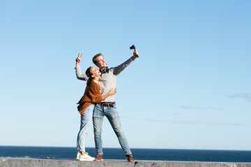 Social media content creation concept. A happy couple recording themselves and vlogging in a sunny day at the seaside.
