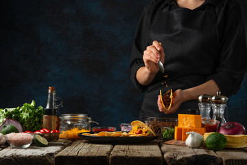 Professional chef in black uniform puts the filling on corn tortilla for cooking tacos on dark blue background. Traditional mexican cuisine. Concept of tasty street food. Frozen motion.