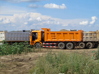 Obraz premium Trucks on the construction site. Road construction. Bright trucks. Summer landscape. Blue sky. Ust-Kamenogorsk (Kazakhstan)