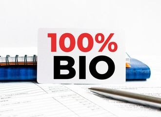 Business card with text 100 percent Bio lying on blue notebook