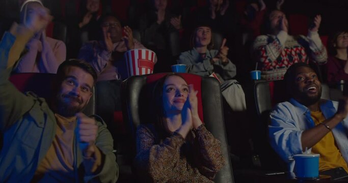 Front view of people applouding at end of good film in movie theatre. Excited people clapping after watching interesting film. Concept of leisure and entertainment