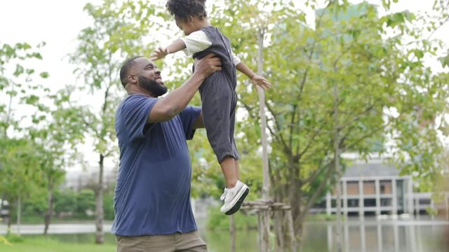 Happy affectionate mixed race family. African man father playing and carrying little daughter at public park. Dad and cute child girl enjoy spending time together in outdoor weekend vacation.