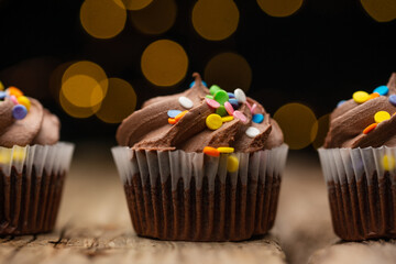 Close-up view of tasty chocolate cupcake on rustic wooden table with yellow lights on black background. Sweet dessert. Bakery concept. Delicious food.