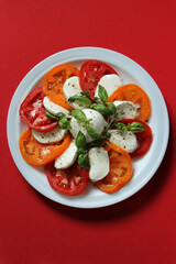 On a plate of salad with mozzarella and tomatoes on a red background