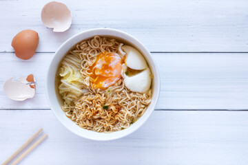 Instant noodles, white cabbage and boiled eggs in a white bowl on a white wooden background. Top View.