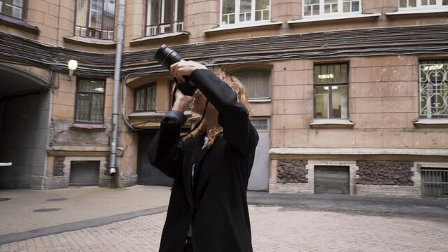 Beautiful woman walks around city and takes photos of old architecture. Action. Female photographer takes pictures of old city architecture. Woman walks through back streets of city