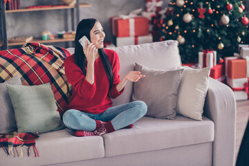 Obraz premium Photo of charming young lady sit sofa hold telephone speak wear red sweater denim jeans socks in decorated living room indoors