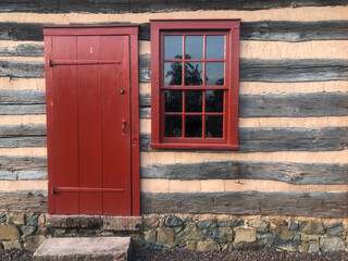Obraz premium Beautiful historic log construction with stone foundation and stepping stone threshold. Full frame image in natural light, with 12-pane window and long hinges.