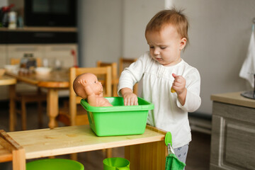 Toddler toddler bathes a toddler doll in a basin of water and a sponge, montessori and earlier...