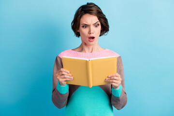 Photo portrait of angry upset woman holding yellow book in two hands with open mouth isolated on pastel light blue colored background