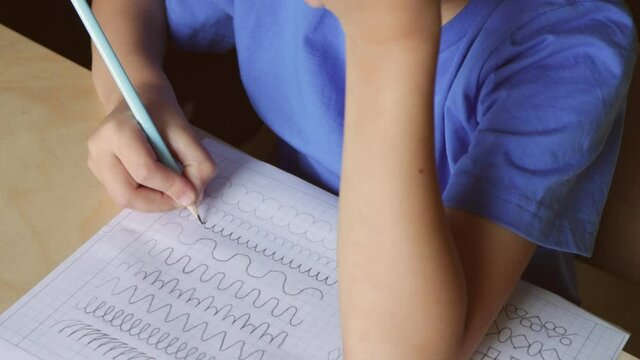 Video of cute boy writing different lines with pencil. Prewriting practice to prepare hands for write letters. Children education concept. View from above
