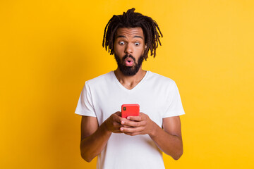 Photo of amazed dark skin guy hold telephone read shock novelty wear t-shirt isolated yellow color...