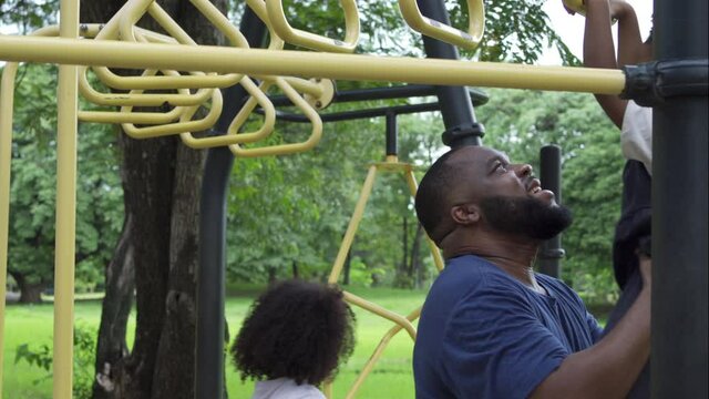 Happy affectionate mixed race family. African man father carrying little daughter playing at playground in the park. Dad and two child girl enjoy and having fun together in outdoor weekend vacation.