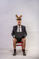 A business man in a shirt, shorts and festive deer horns works on a laptop.