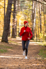 Adult caucasian slim woman in red sportswear and a cap jogging in the forest in autumn outdoor, vertical photo, selective focus