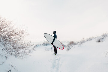 Snowy winter and surfer with surfboard. Winter and surfer in wetsuit.