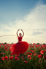 Pretty young woman in red dress dancing like ballerina in the poppy flowers meadow.