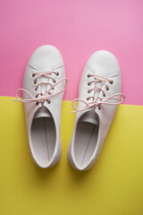Pair of white gumshoes on pink-yellowl background.