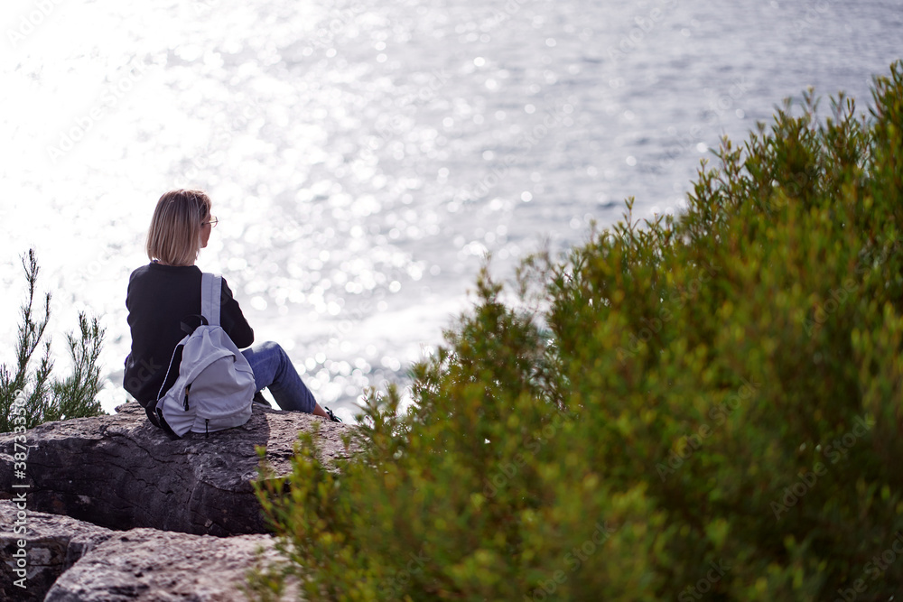 Wall mural Tourism concept. Young traveling woman with rucksack enjoying ocean view.