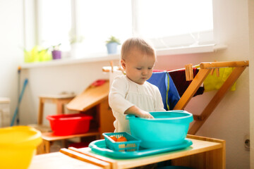 Toddler child plays with water in a basin, developing sensory activities with water and objects, montessori and earlier child development, toddler independence
