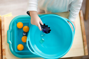 Toddler child plays with water in a basin, developing sensory activities with water and objects,...