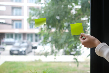 Cropped shot of hand putting sticky notes on glass window for planning analysis in office.