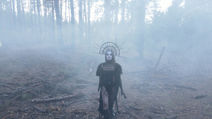 Woman in image of witch walks across dark and foggy forest.