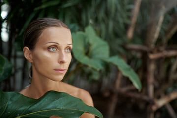 Close up outdoor portrait of young beautiful woman against green tropical leaves.