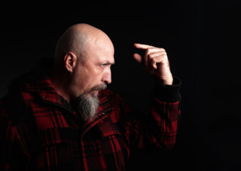 disgruntled, wary middle-aged man with a gray beard in a checkered red cloth jacket with a shaved head.