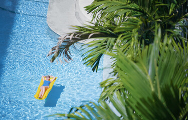Enjoying suntan. Tropical vacation concept. Top view of young woman on the yellow air mattress in...