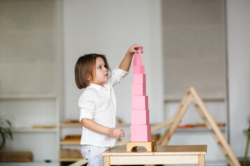 child girl playing with pink tower, developing sensory activities in montessori and earlier child development, kids independence - obrazy, fototapety, plakaty